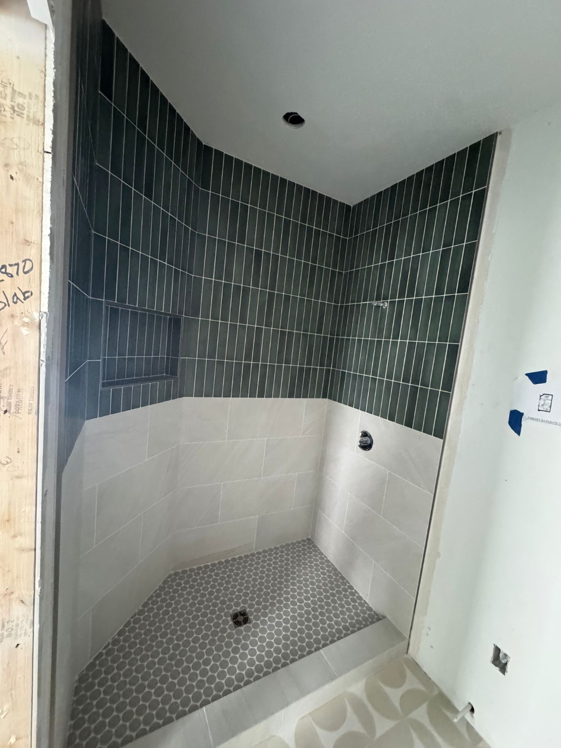 Green vertical shower tile above white tile with a recessed niche and penny-round floor during installation